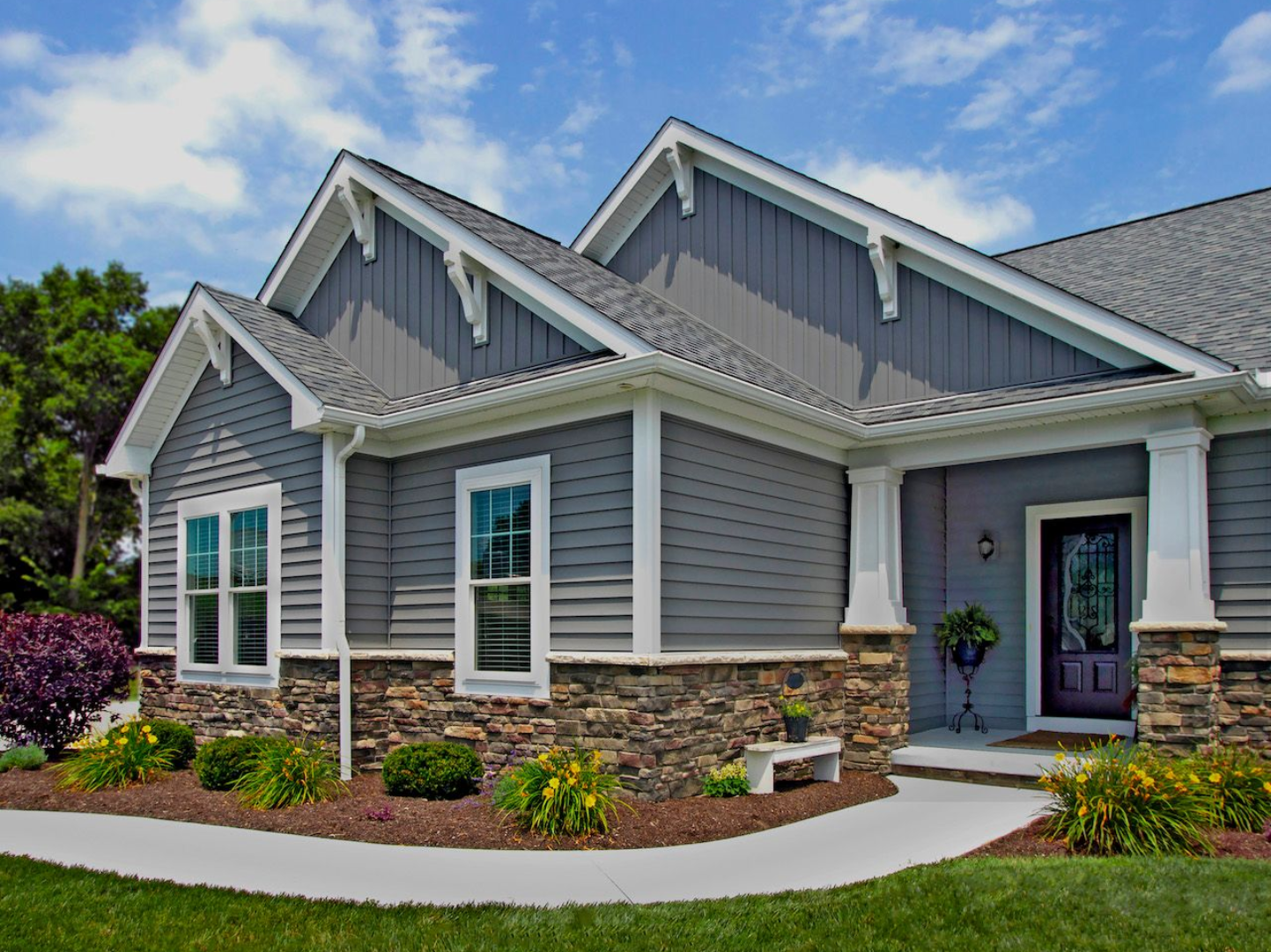 Gray house with stone base, white trim, and blue sky.