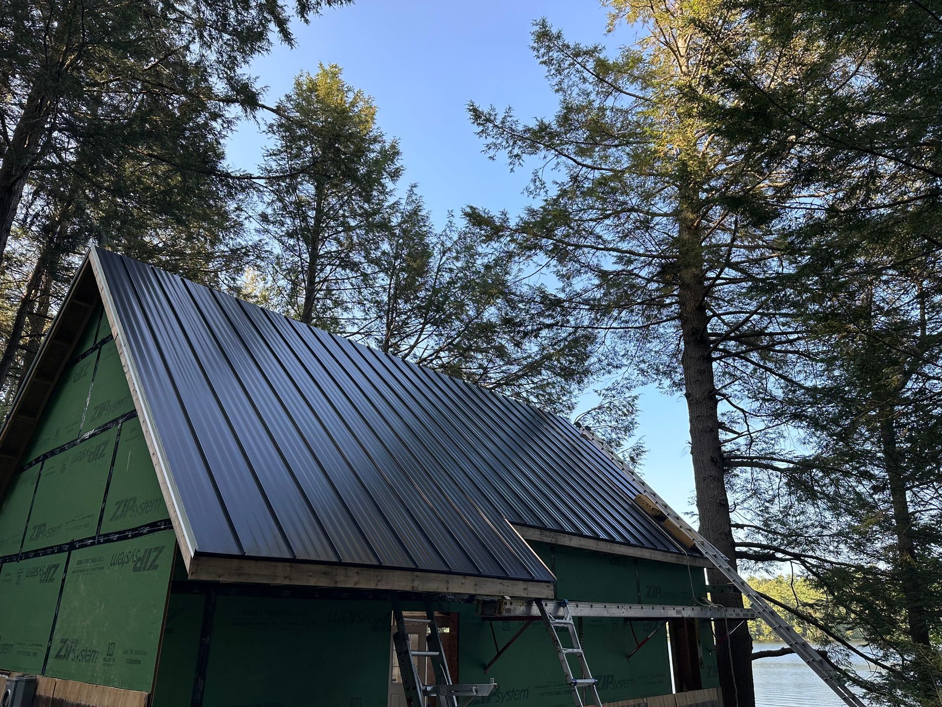 Small cabin under construction with black metal roof and green siding, surrounded by trees.