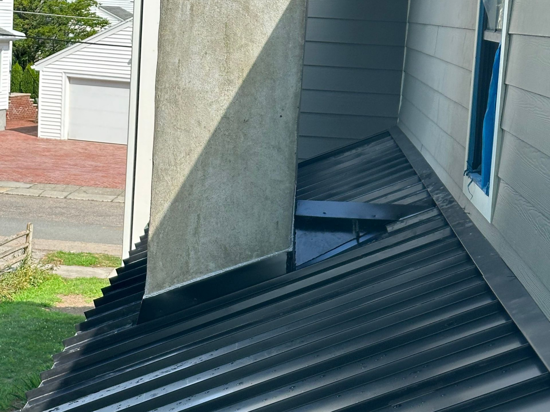 Black metal roof with a chimney and part of a house.