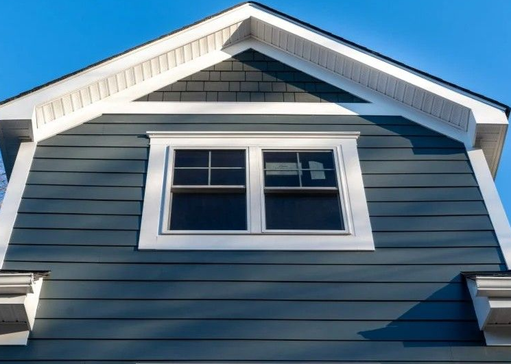 Blue siding gable with white trim, window, and dark shingles against a blue sky.