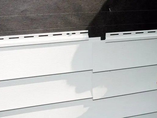 White vinyl siding with top section of trim against dark gray wall.