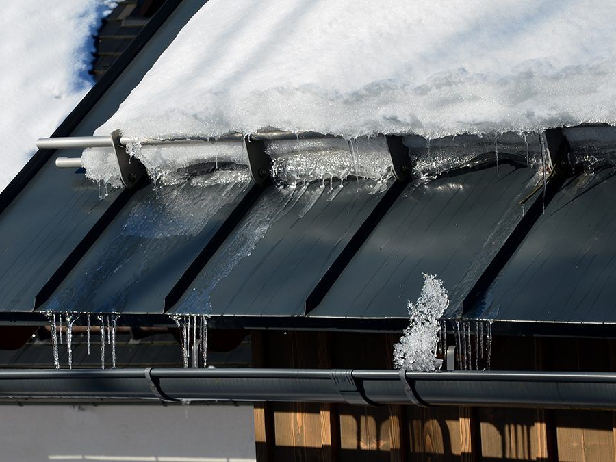 Snow and ice on a dark roof with icicles hanging from the edge and a black gutter below.
