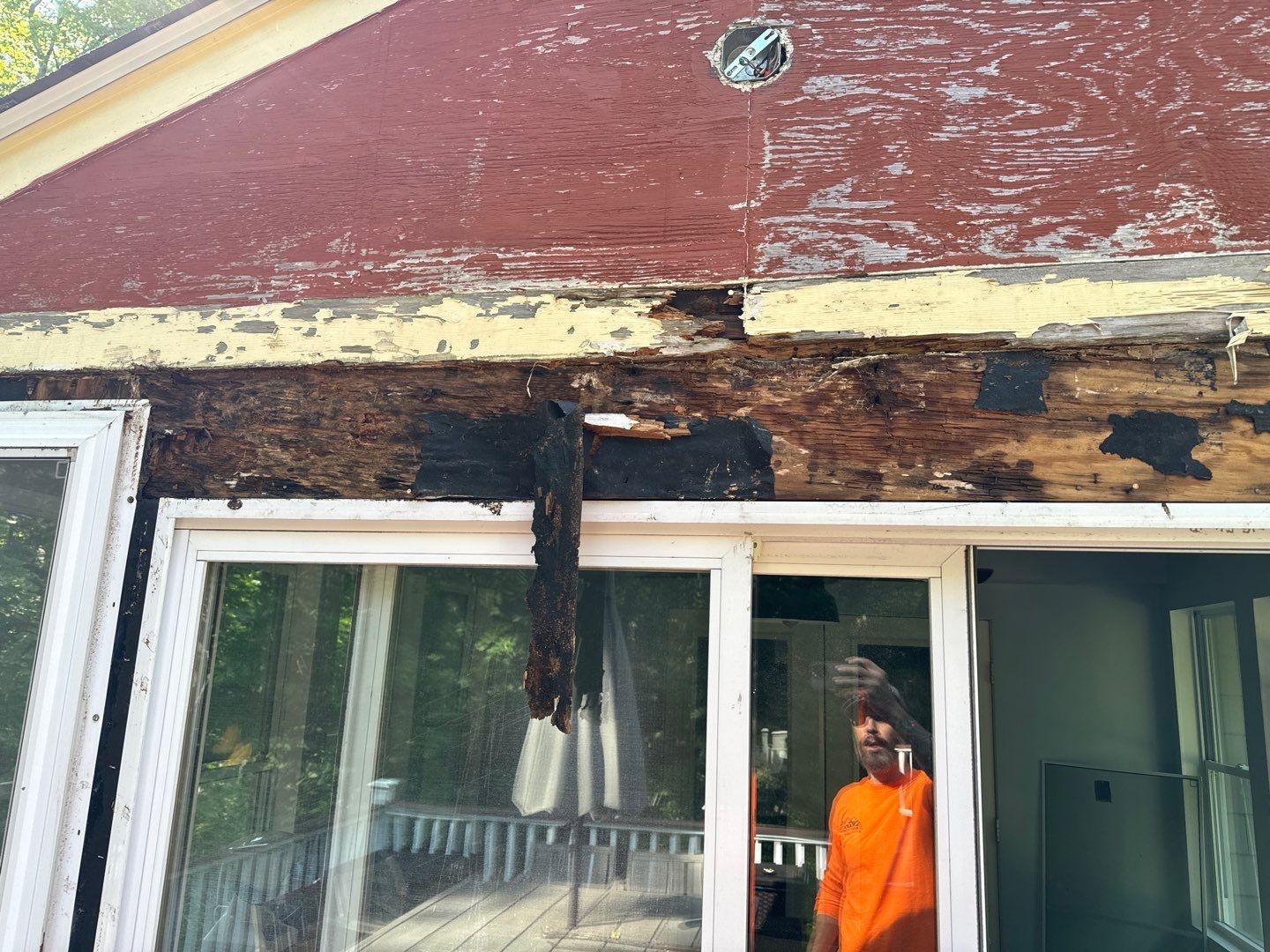 Damaged house eaves above sliding glass doors; red paint peeling, person in orange shirt.