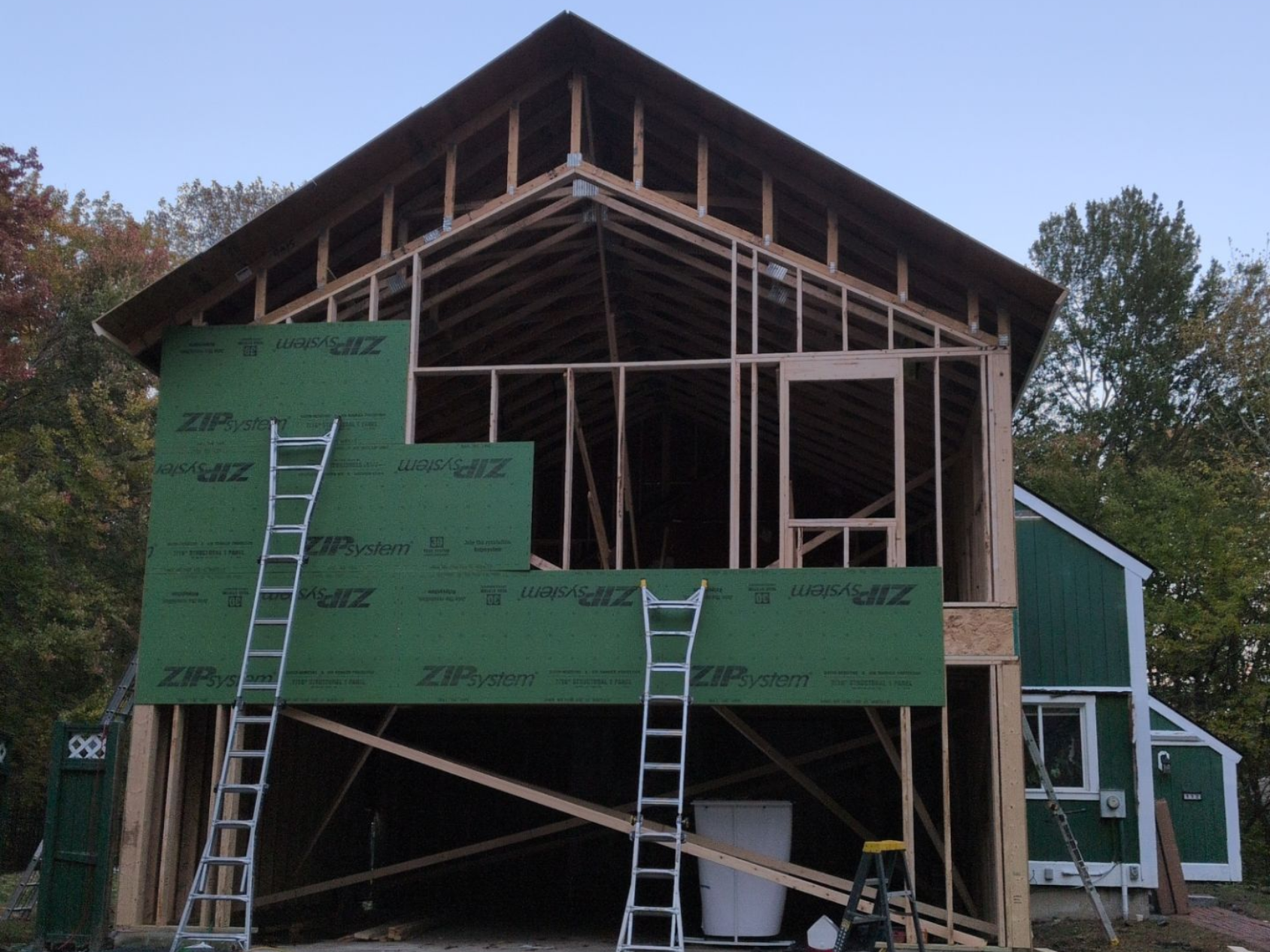 Framing of a two-story building addition. Green sheathing and ladders are visible.