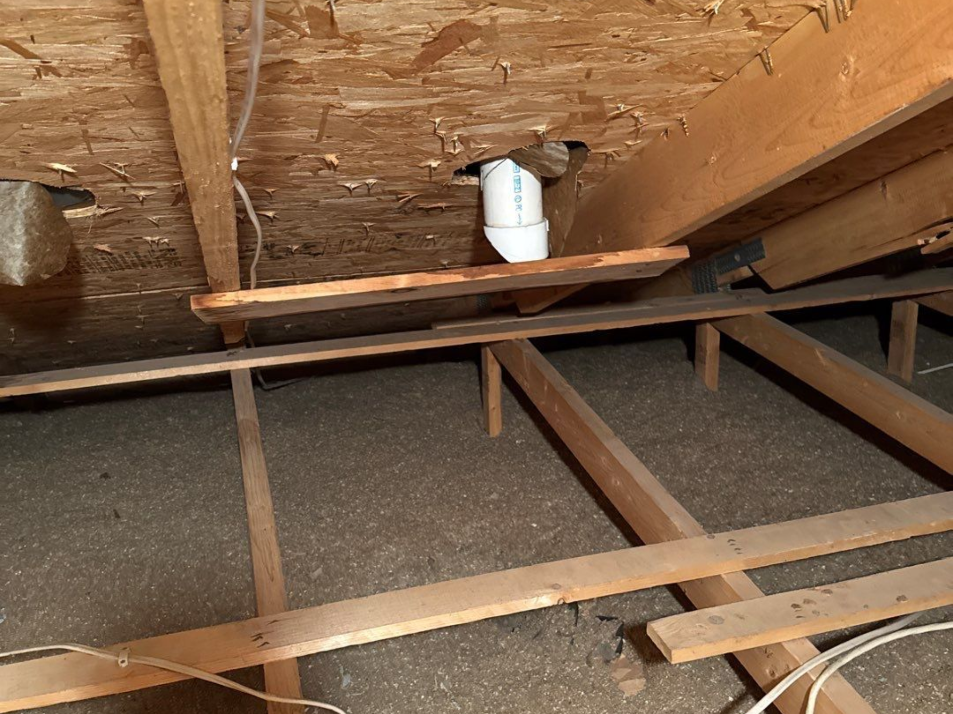 Attic view with wooden rafters, insulation, and a white pipe extending through the ceiling.