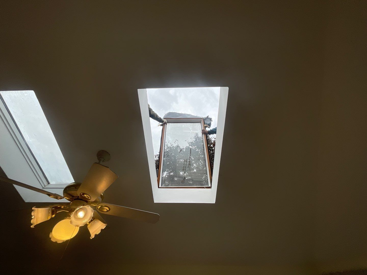 Ceiling with open skylight and ceiling fan; cloudy sky visible.
