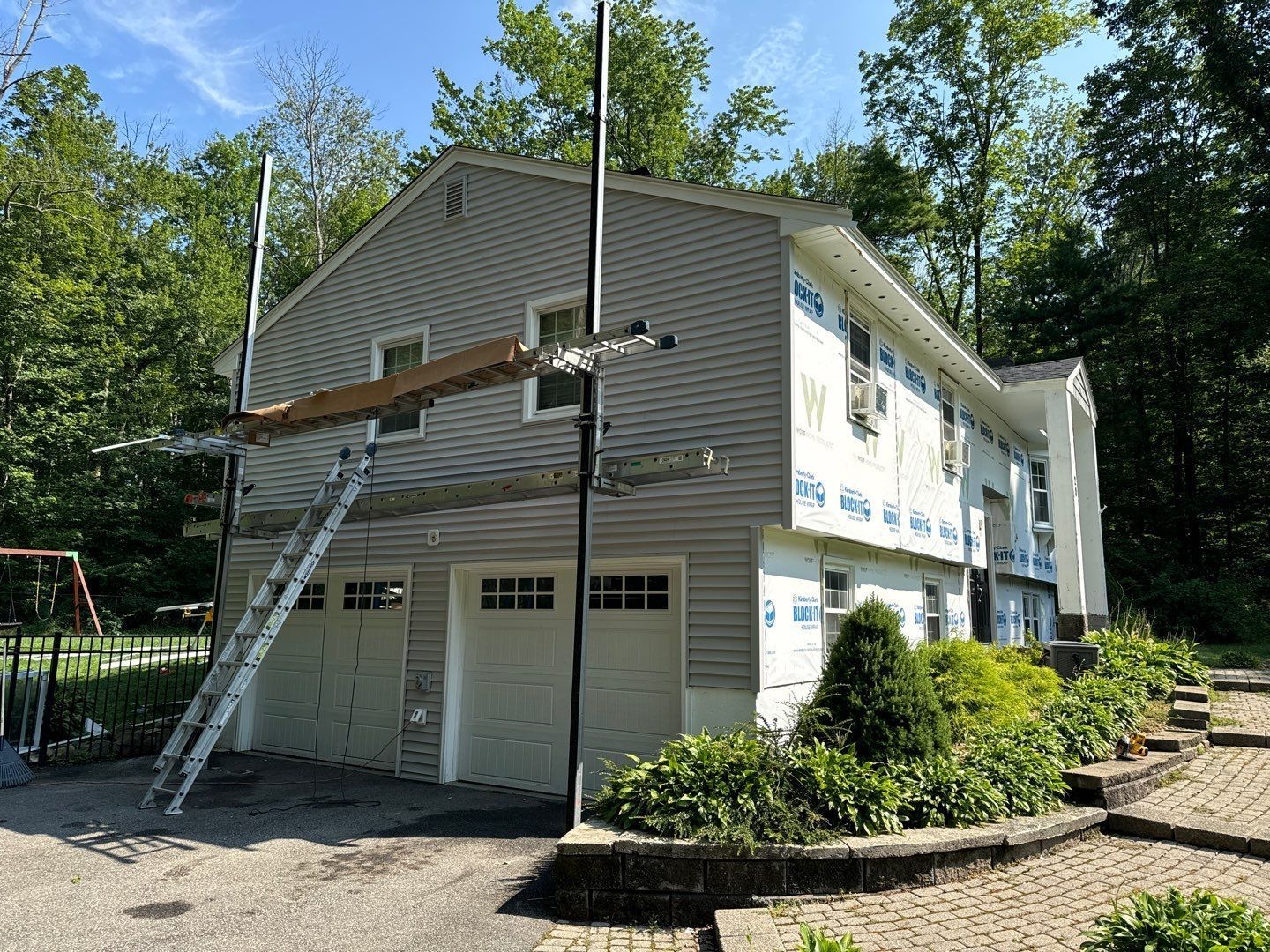 House with gray siding under renovation; scaffolding and ladder are set up.