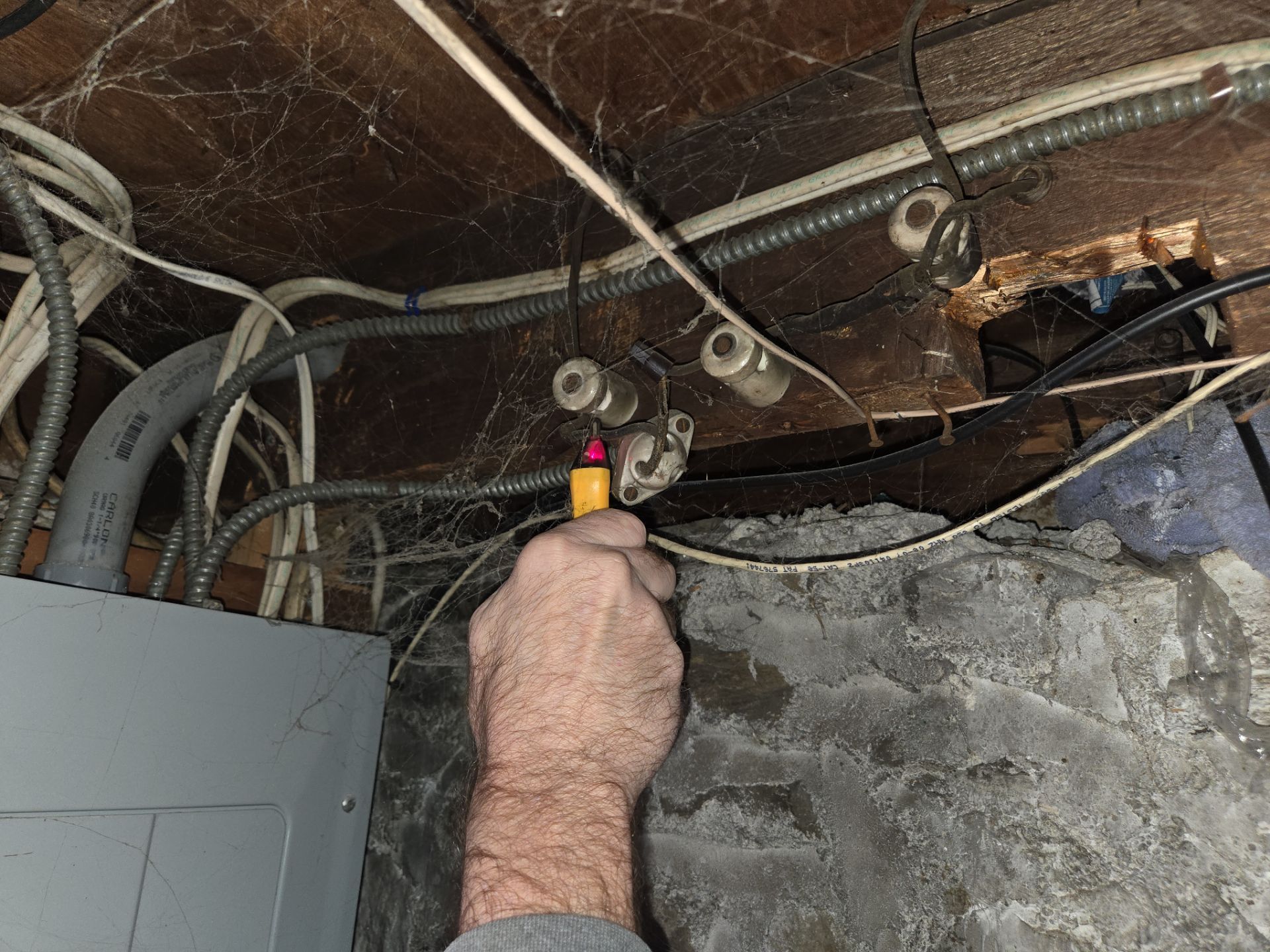 Person testing electrical wiring with a voltage tester in a basement.