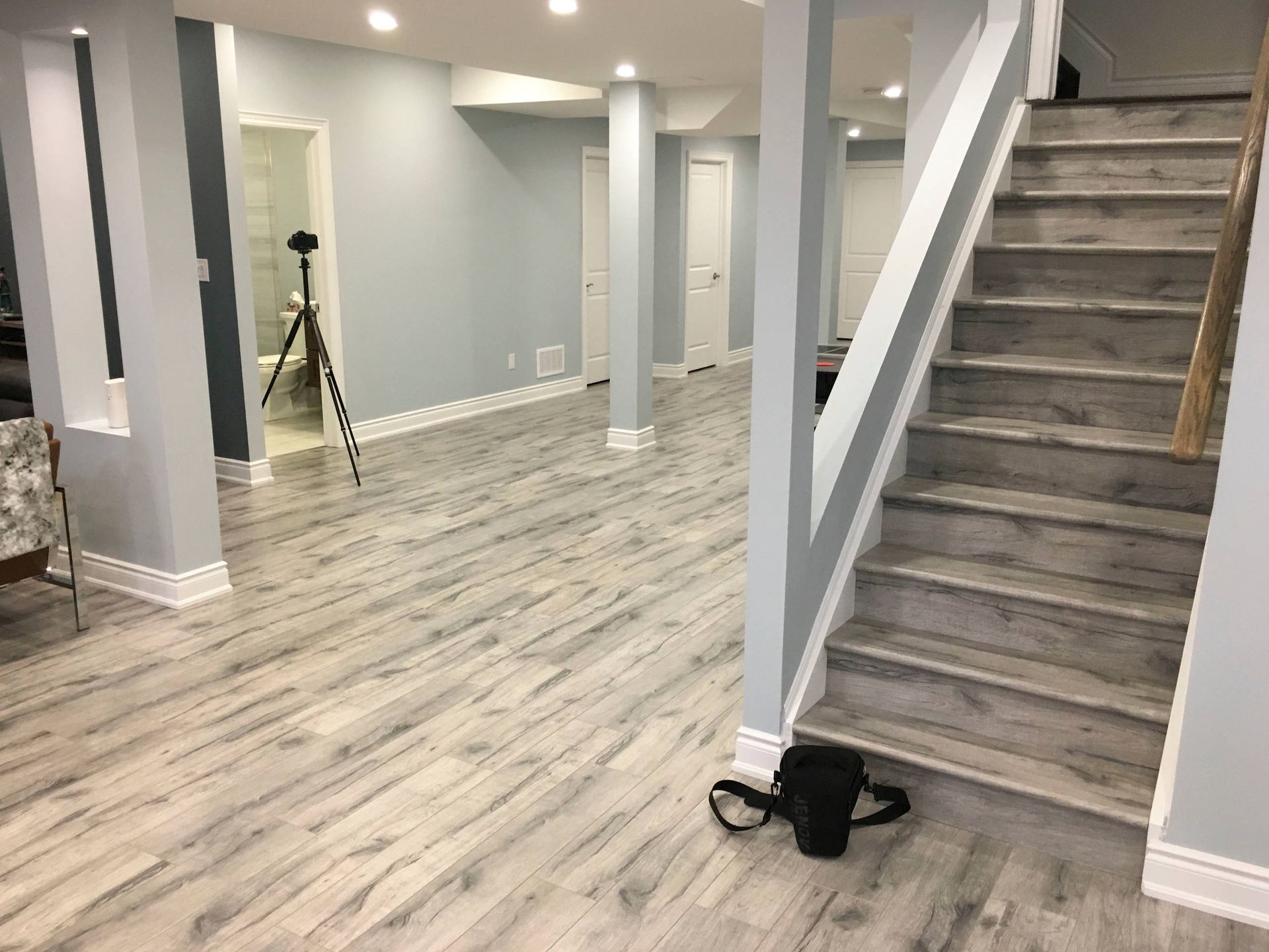 Finished basement with light gray wood-look flooring, light blue walls, and a staircase.