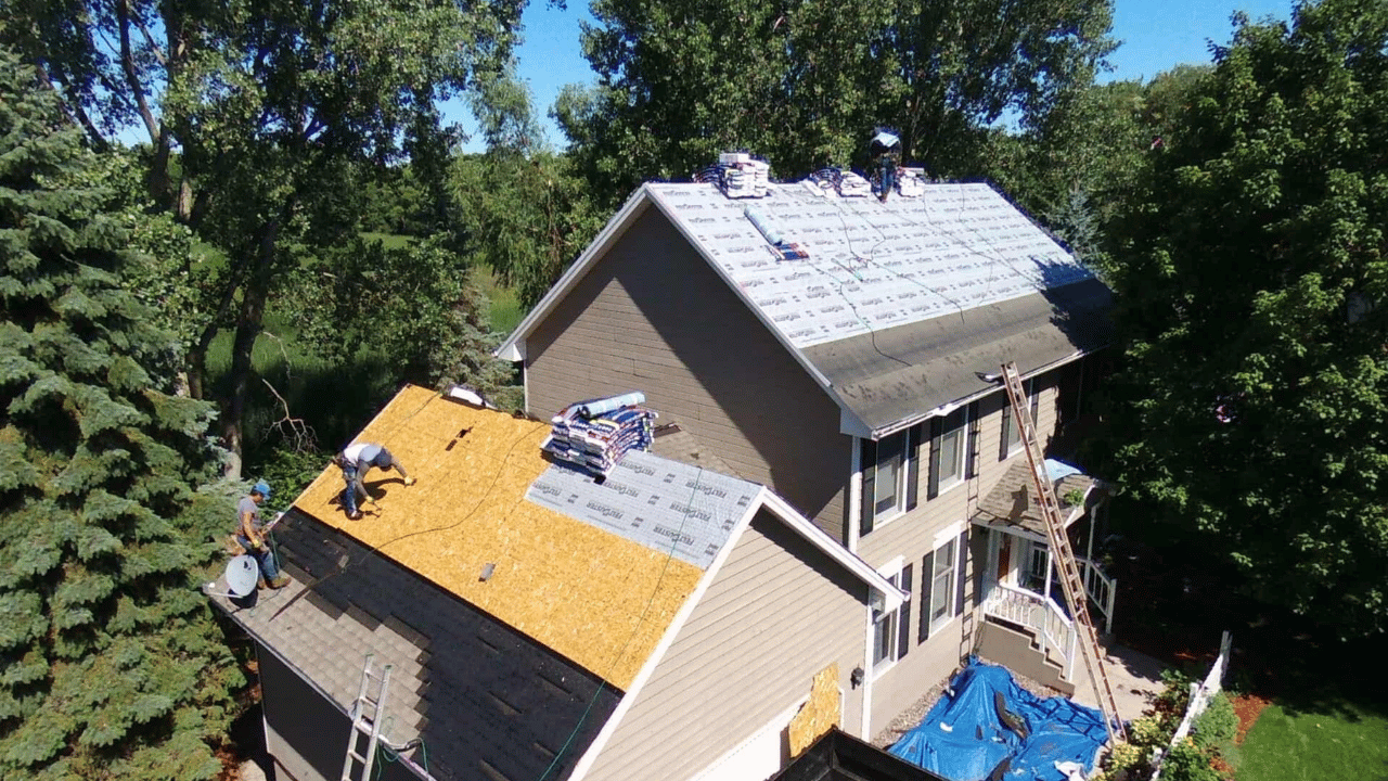 Roofers working on a house roof replacement; shingles, ladders, and tools are visible.
