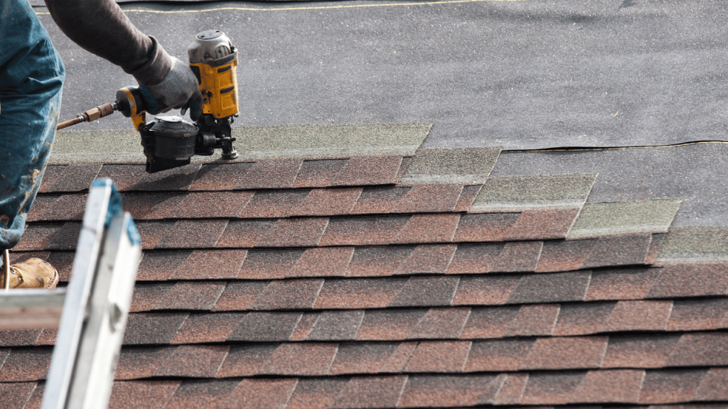 Roofer using a nail gun to install asphalt shingles on a roof.