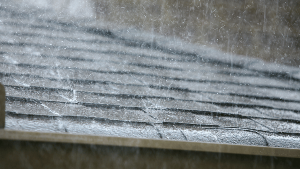 Rain falling heavily on a dark gray shingled roof, creating a textured surface.