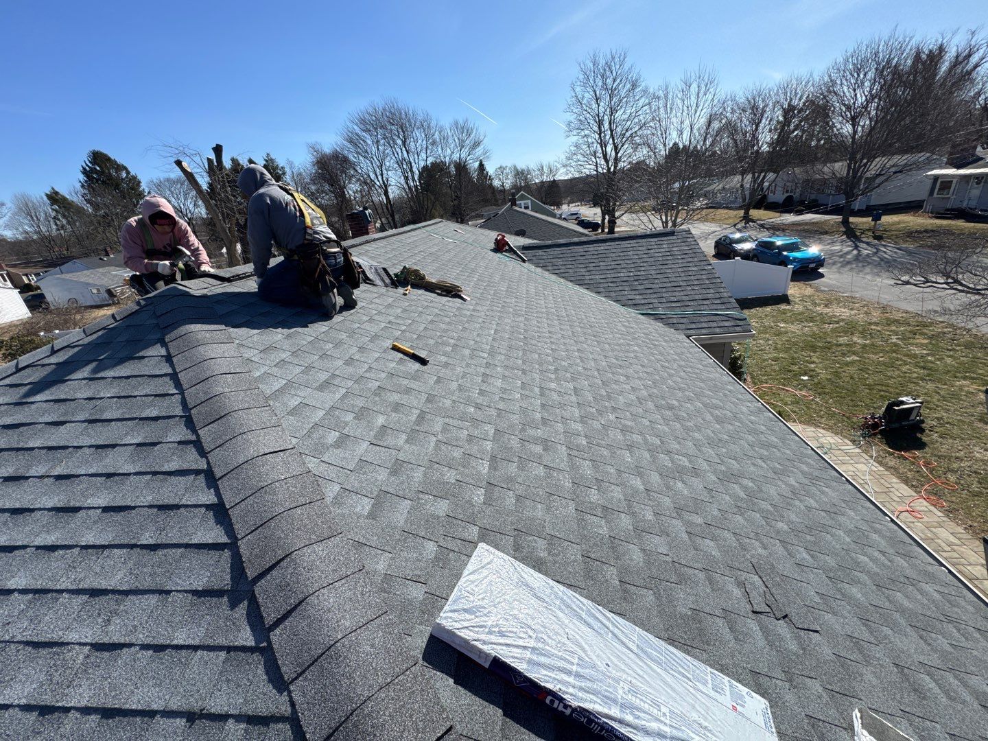 Two roofers working on a gray shingled roof on a sunny day.