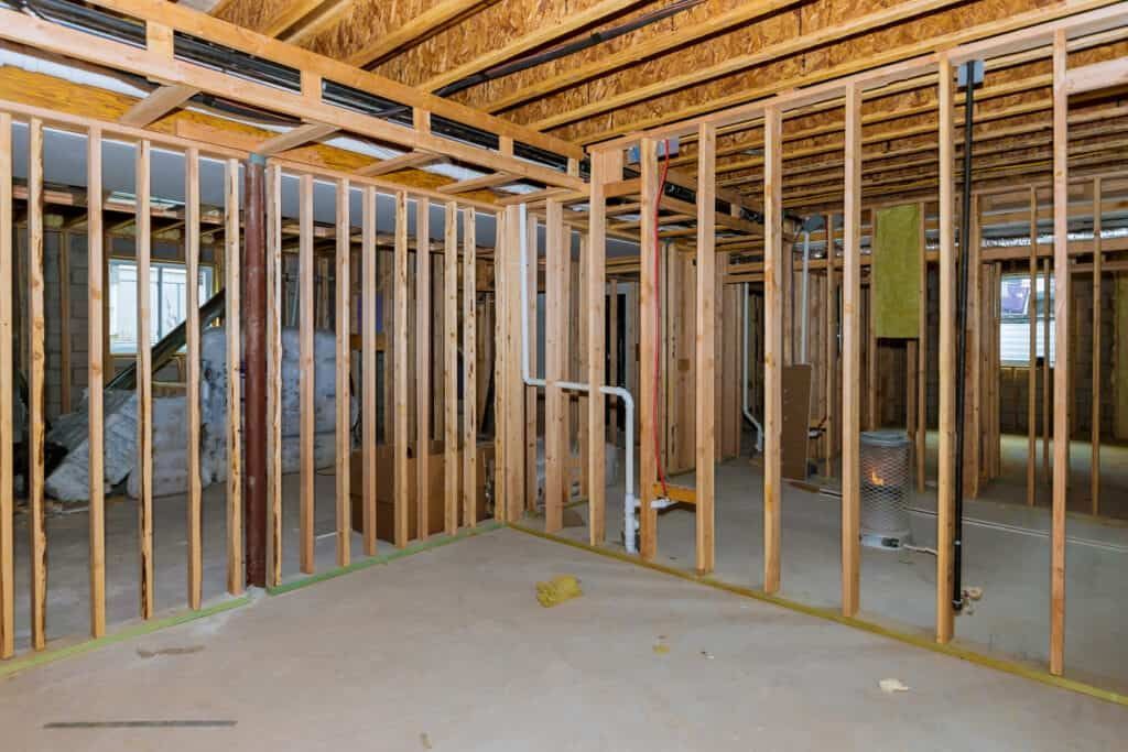 Interior of unfinished room in basement with exposed wooden studs and ceiling beams.