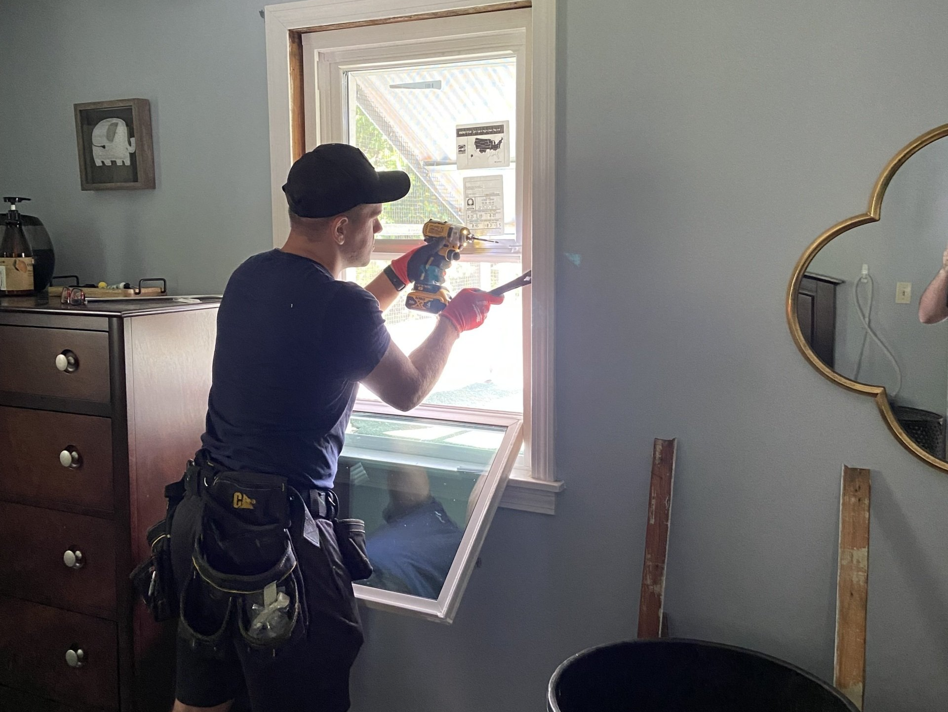 Person in black clothing removing a window; interior setting with dresser and mirror.