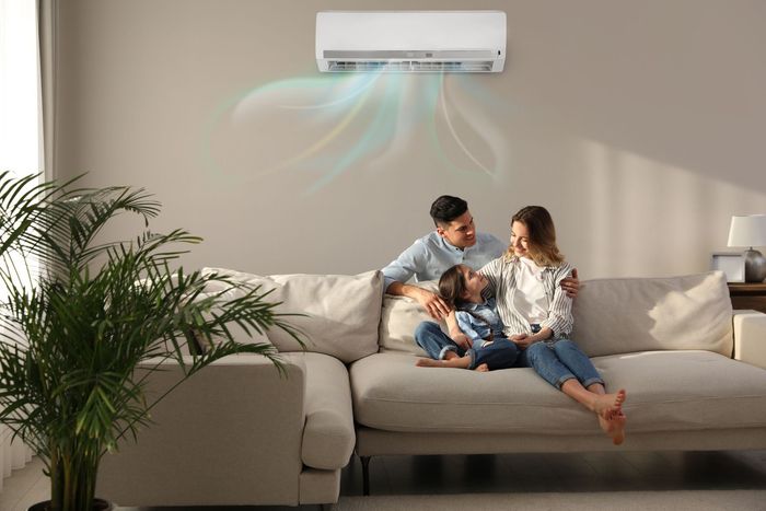 A family is sitting on a couch under an air conditioner in a living room.