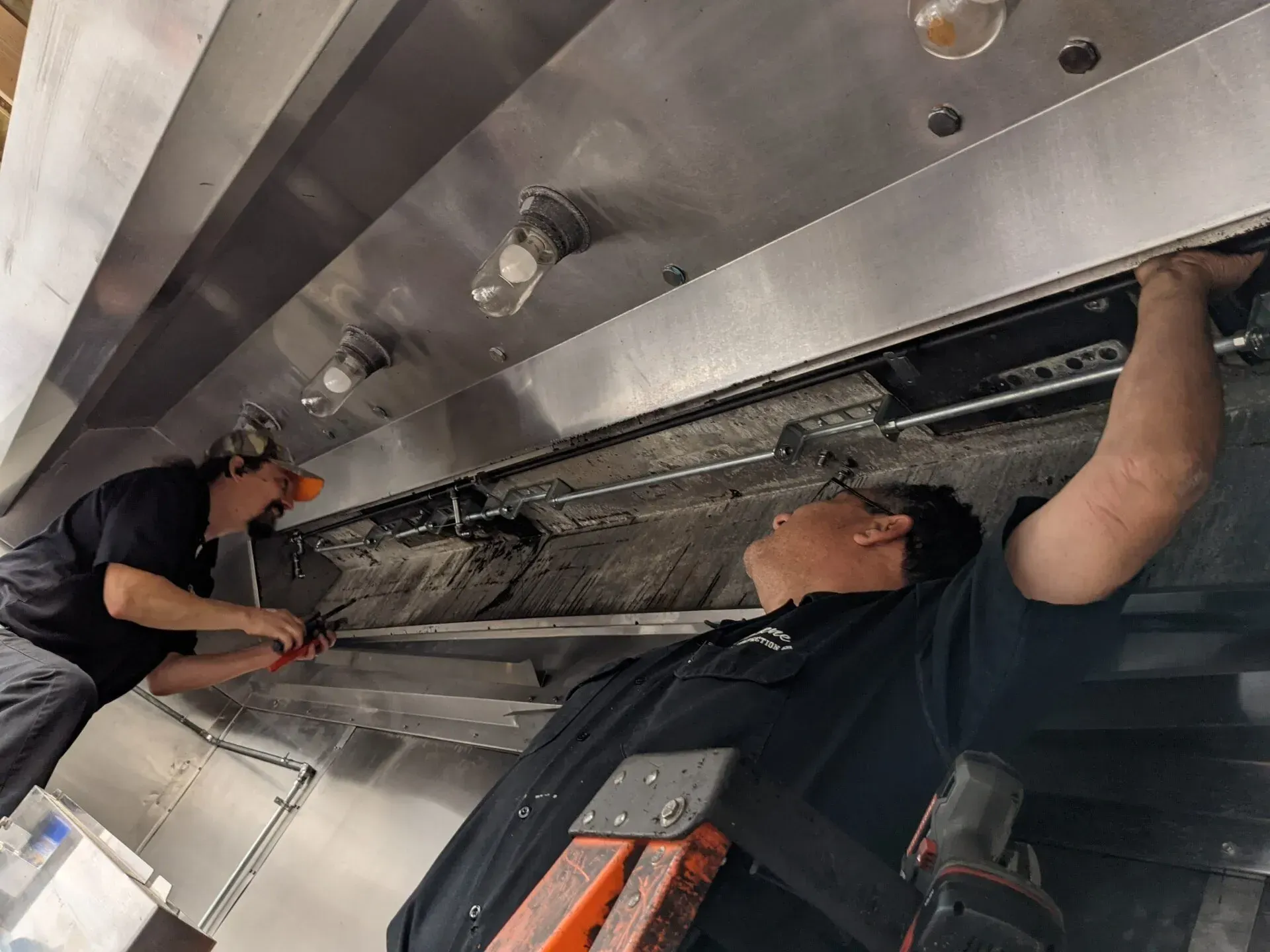 Two men are working on a stove in a kitchen.