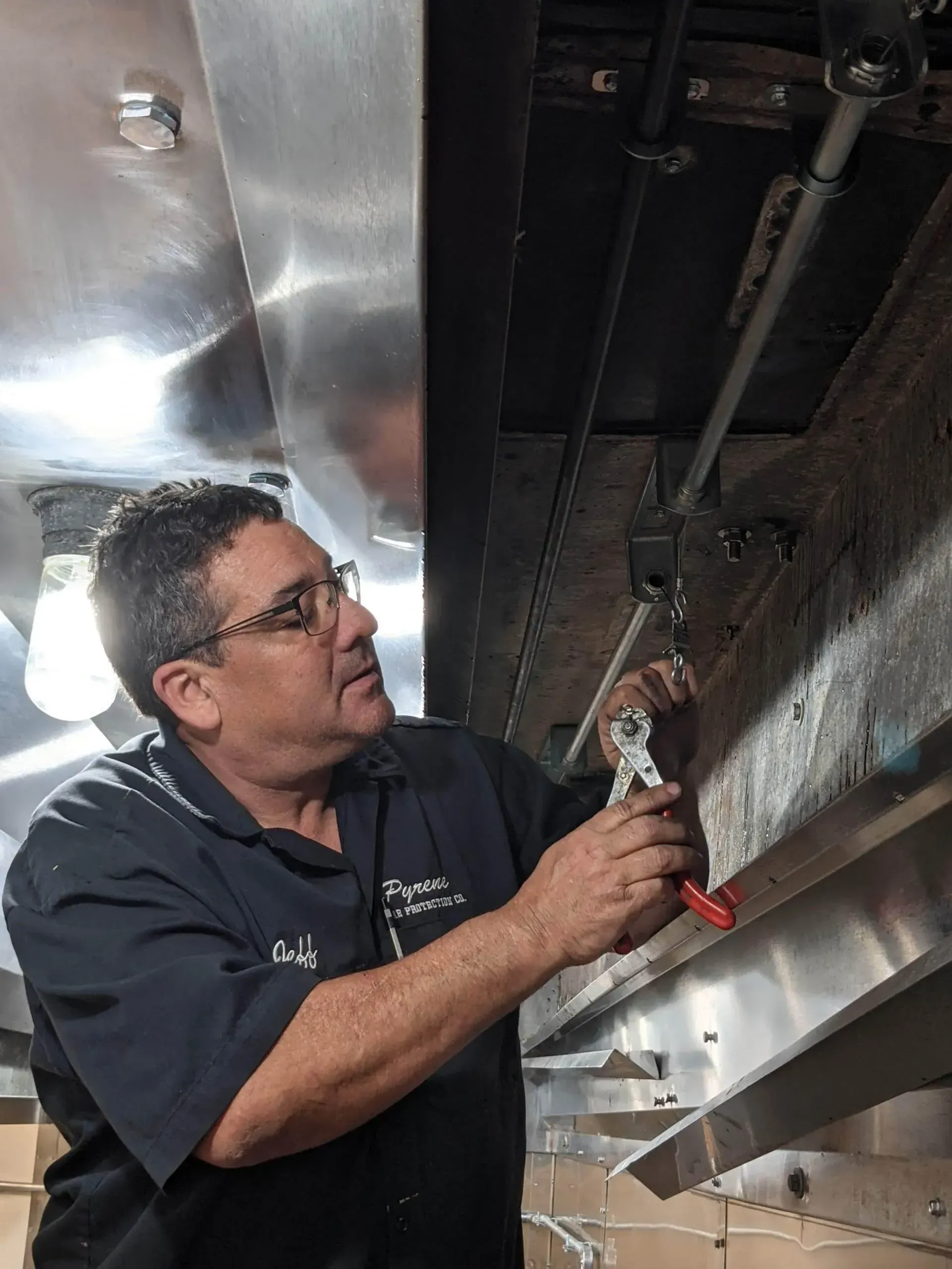 A man is working on a pipe with a wrench in a kitchen.