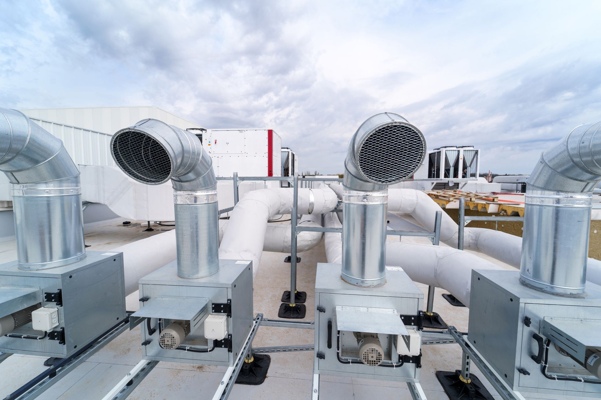 Rooftop HVAC system with silver vents and pipes against a cloudy sky. Rooftop HVAC system with silver vents and pipes against a cloudy sky.
