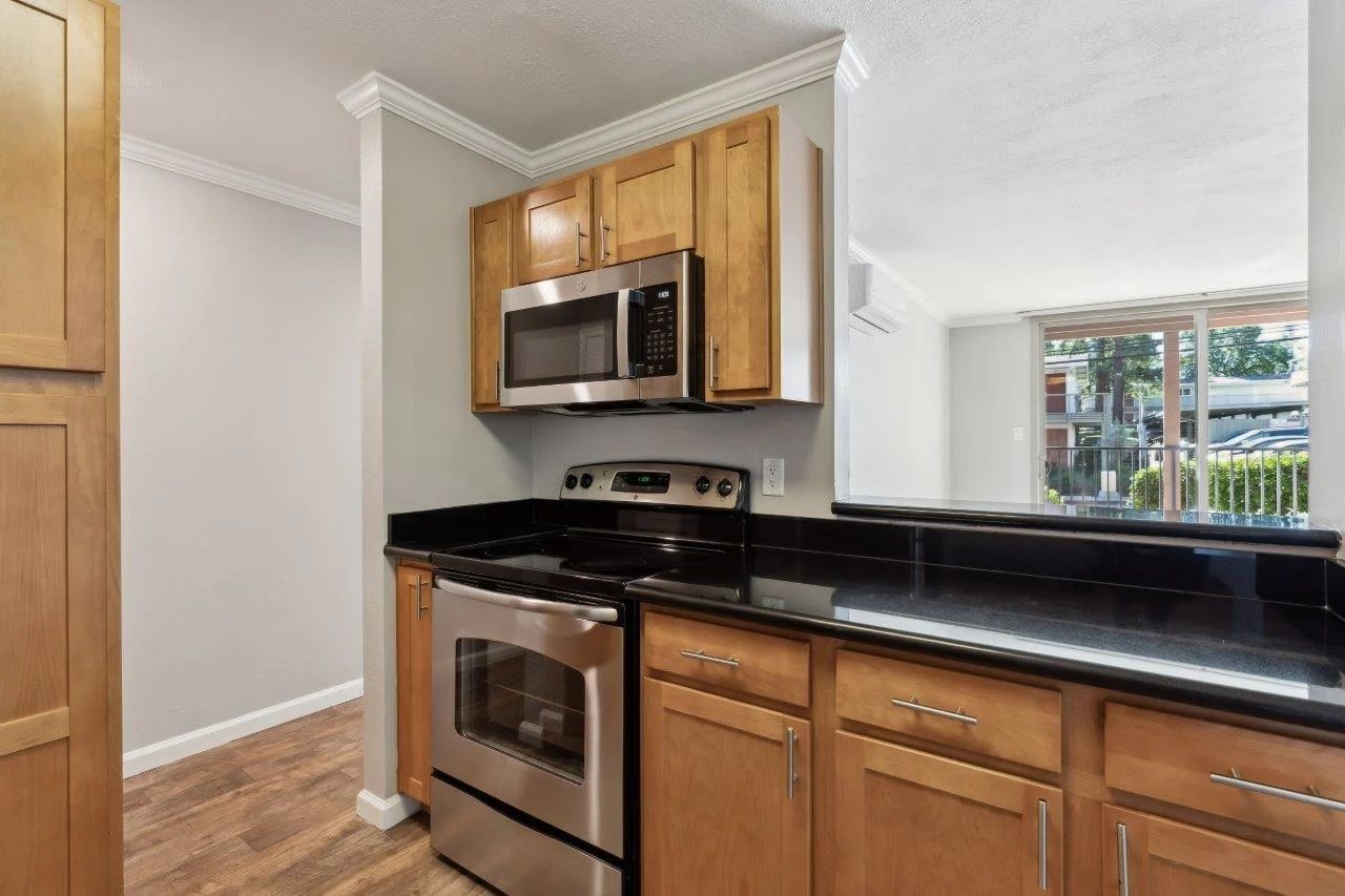 Kitchen with stainless steel appliances, wooden cabinets, black countertops, and a view of an outdoor balcony.