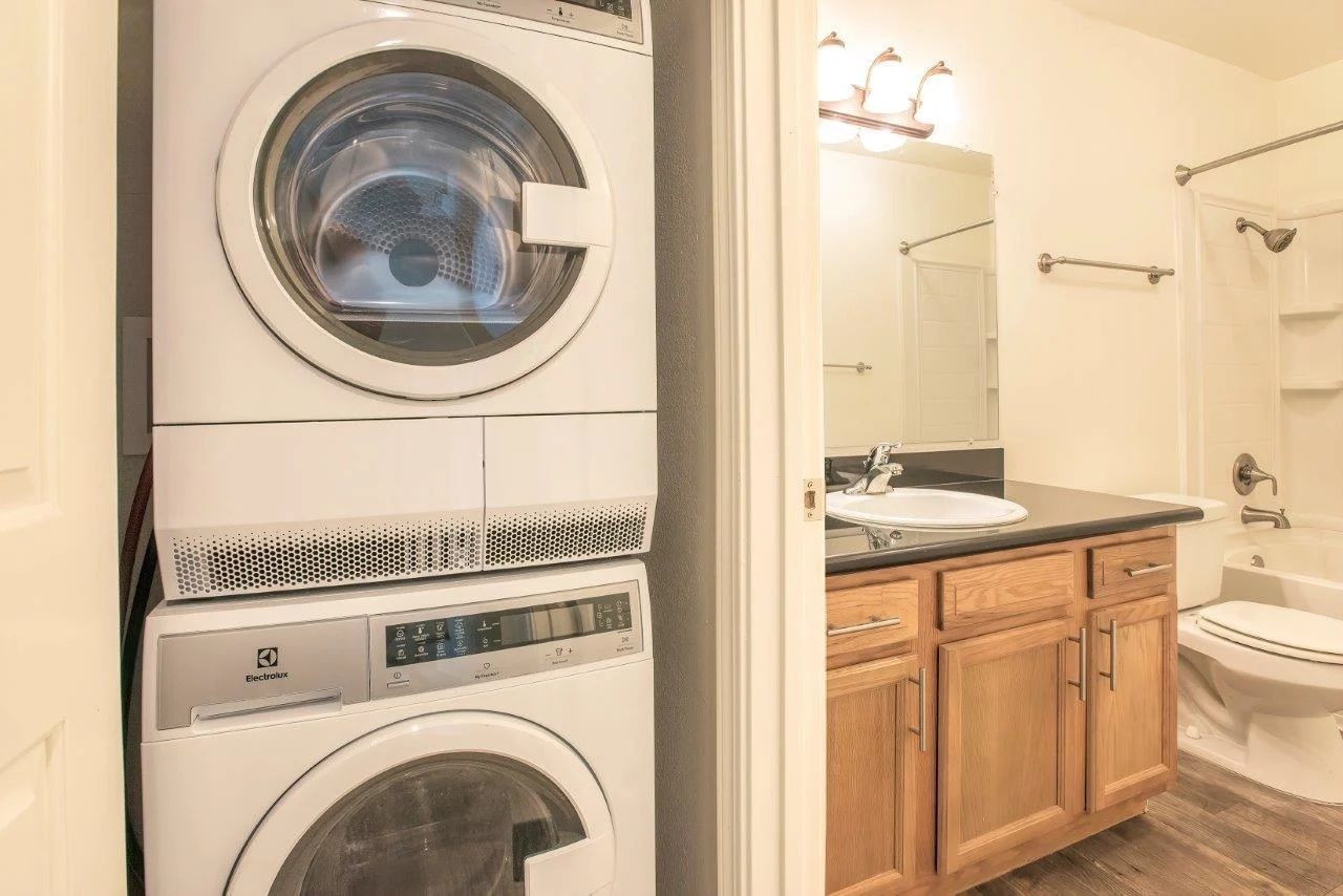 Stacked washer and dryer next to a bathroom with a vanity, mirror, and toilet.