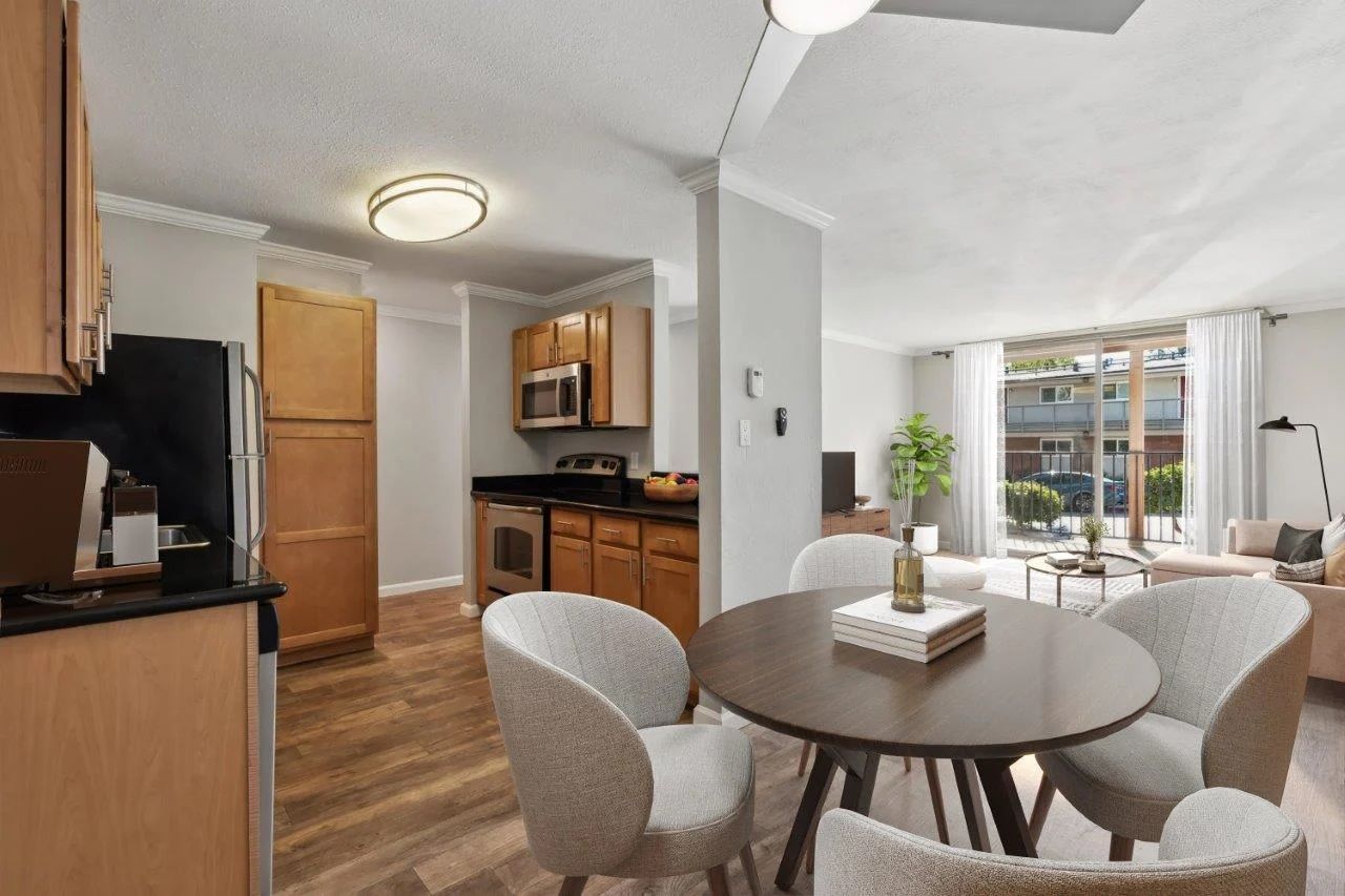 Kitchen and dining area with table and chairs, connecting to a living room with natural light.