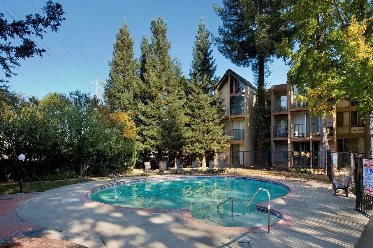 Pool in front of a three-story building with trees and blue sky.