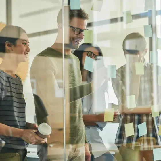 A group of people are standing in front of a glass wall with sticky notes on it.