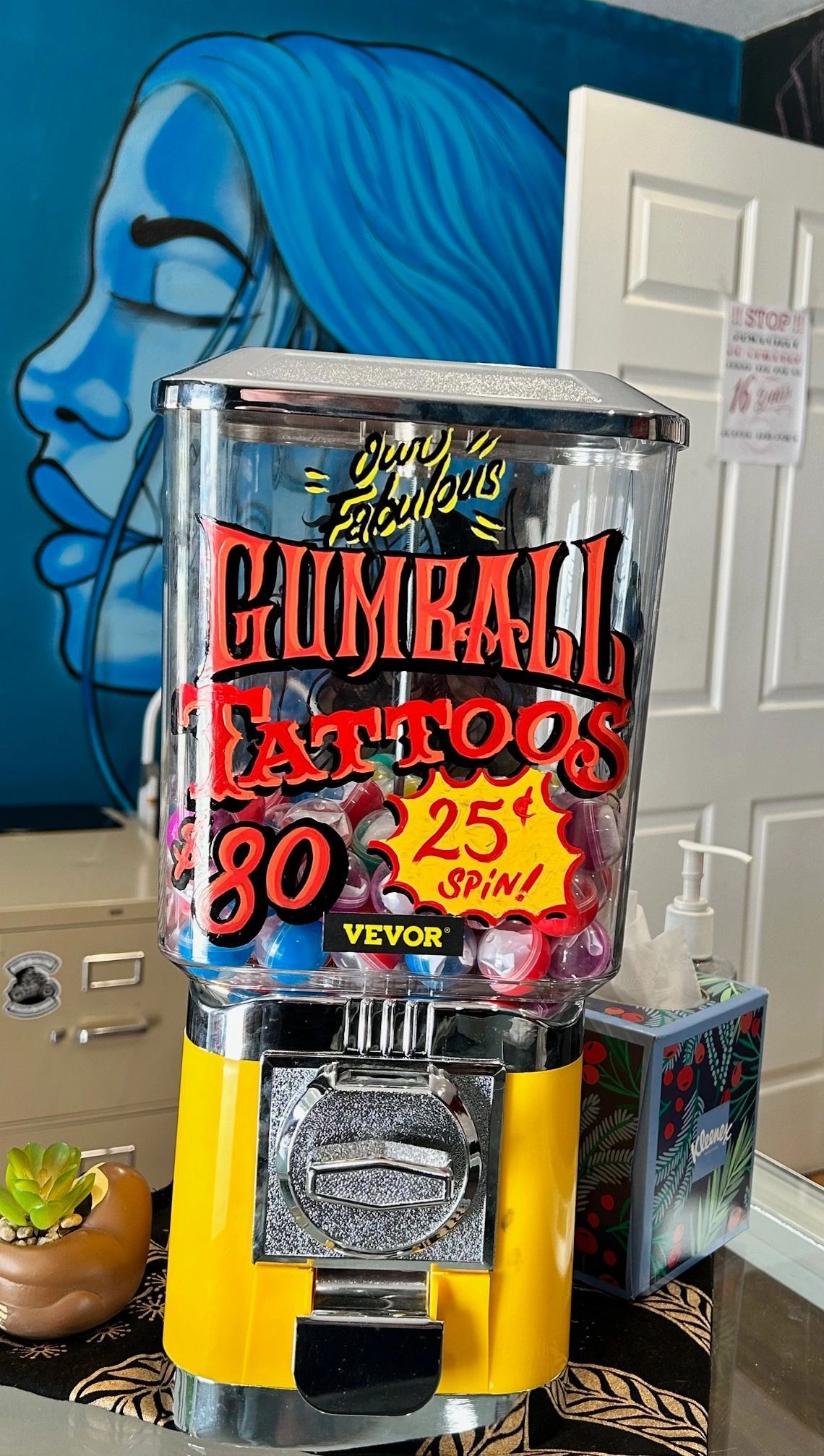 A gumball machine is sitting in a room next to a door.