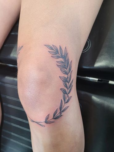 A woman has a tattoo of a laurel wreath on her knee