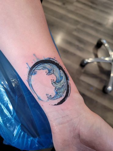 A person has a tattoo of a wave in a circle on their wrist.