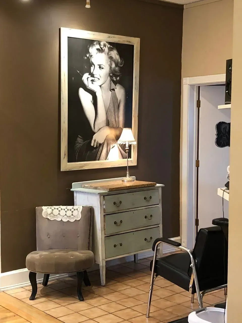 A room with a chair, dresser, and a picture of a woman on the wall.
