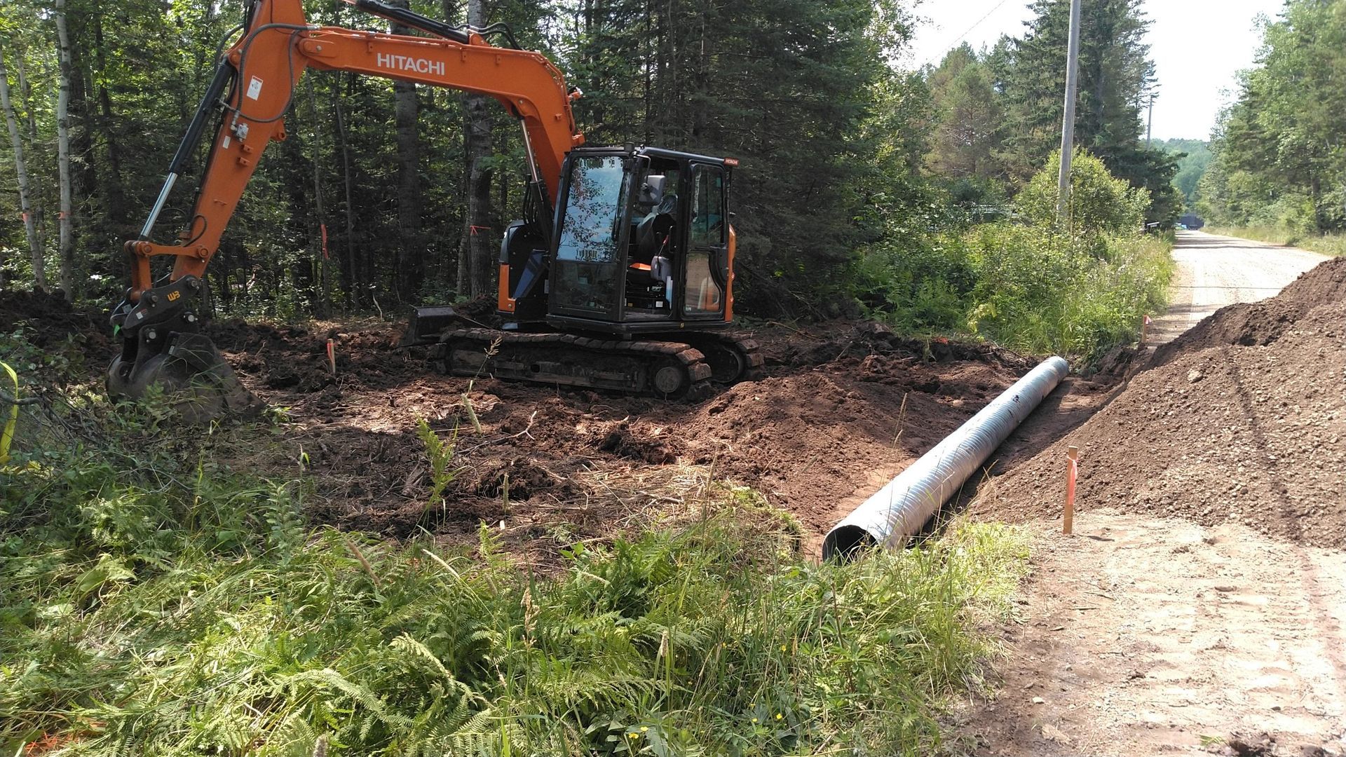 An excavator is digging a hole in the dirt next to a pipe.