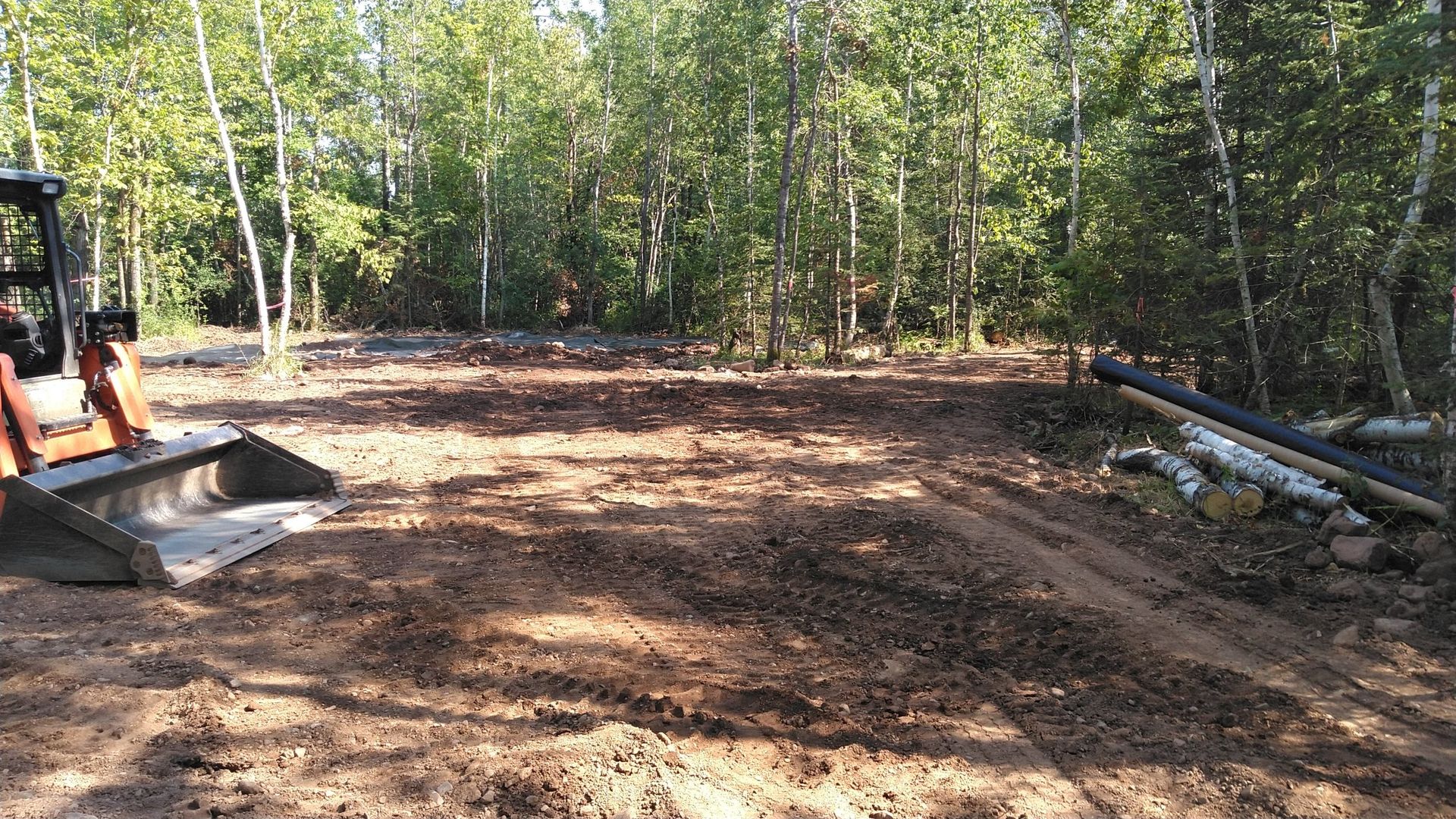 A bulldozer is sitting in the middle of a dirt field in the woods.