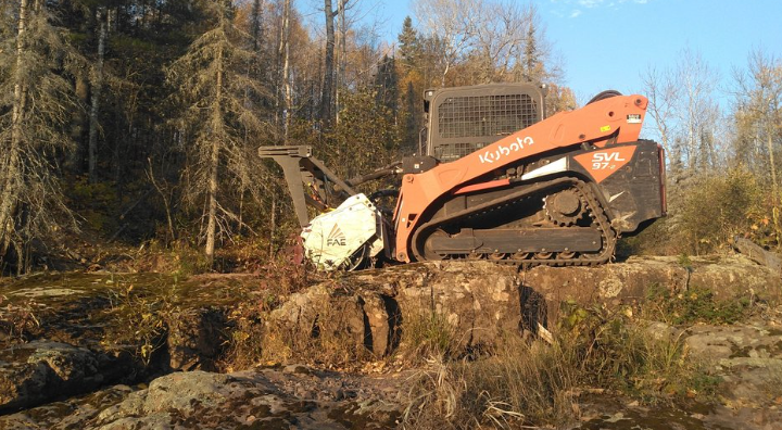 A bulldozer is sitting on top of a rock in the middle of a forest.