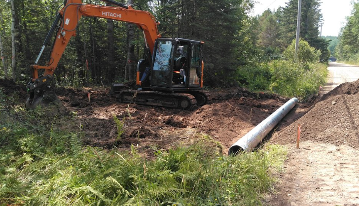 An excavator is digging a hole in the dirt next to a road.