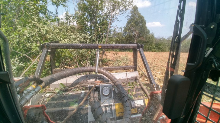 A tractor is driving through a field with trees in the background.
