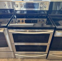 Stainless steel double-oven electric range with black cooktop and digital controls, flanked by other appliances.