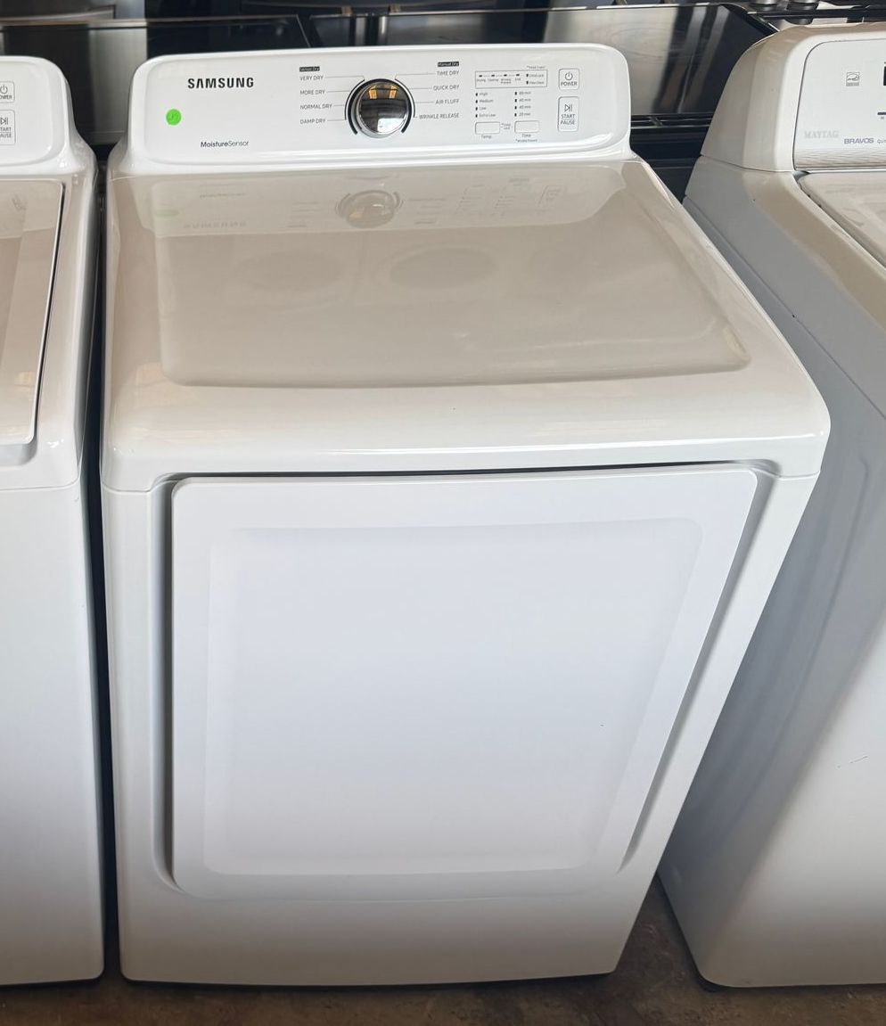 White Samsung dryer with top-mounted controls and a front-loading door, situated between two other white appliances in a store setting.