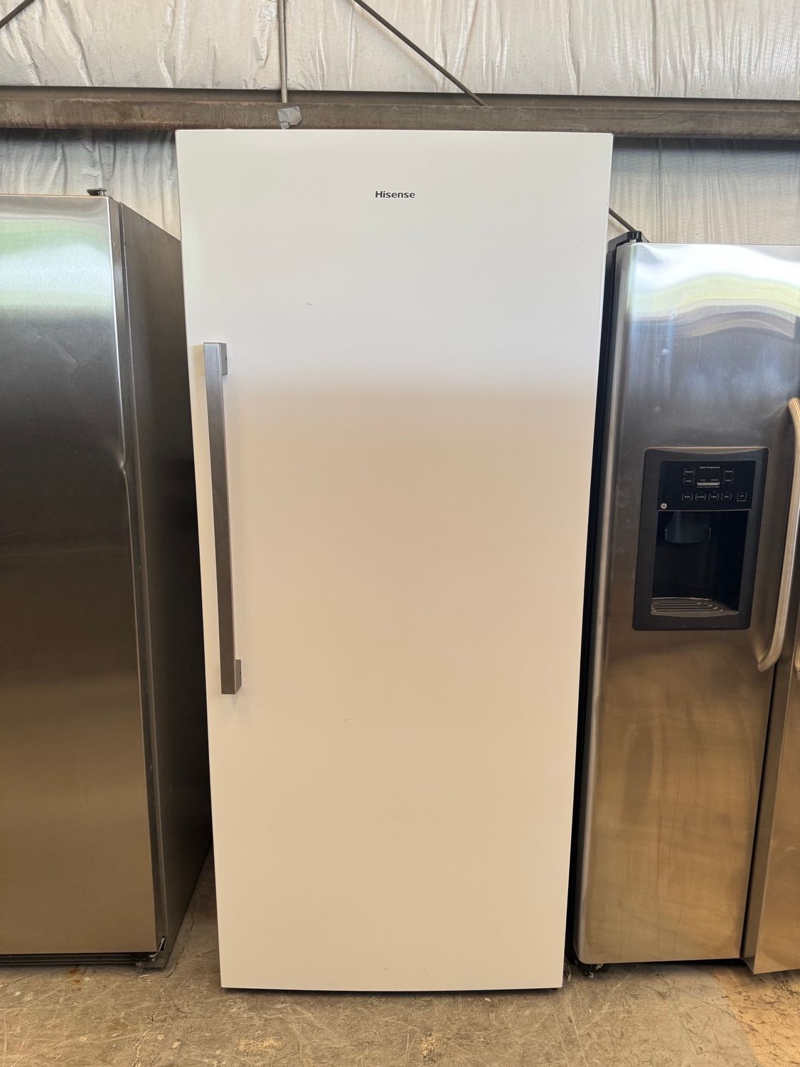 White upright freezer with a stainless steel handle, flanked by two stainless steel refrigerators.