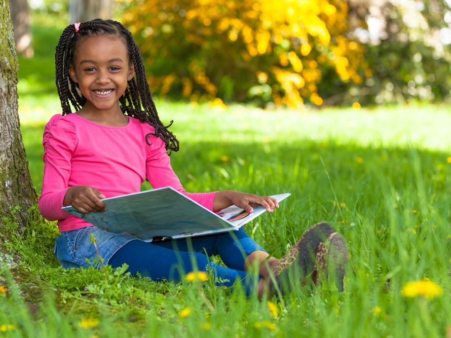 A little girl is sitting under a tree reading a book