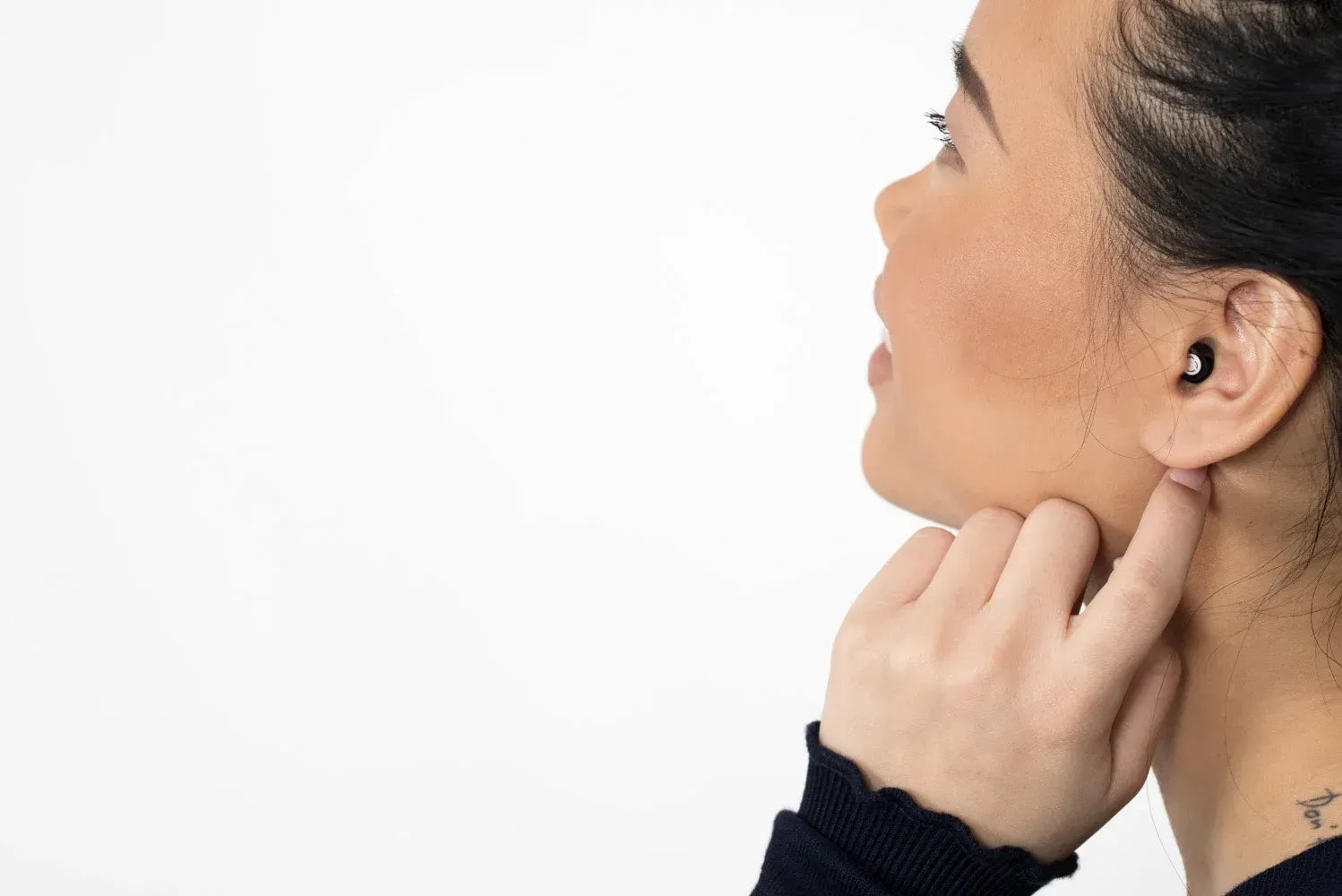Woman with a hearing aid in her ear, touching her ear and looking upward. White background.