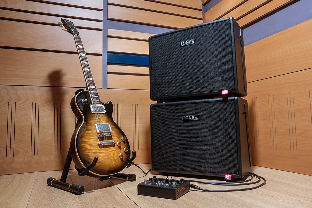 Electric guitar leans against stand next to two black amplifier cabinets in a recording studio.