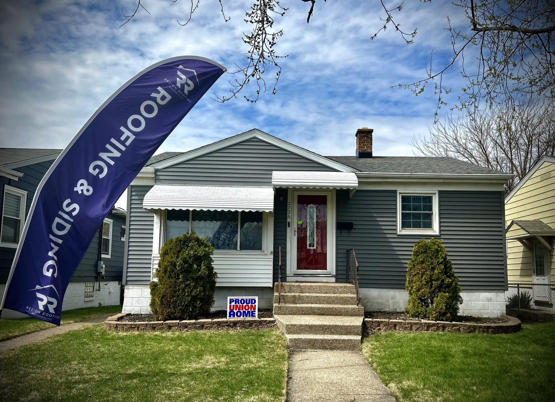 A house with a roofing and siding sign in front of it