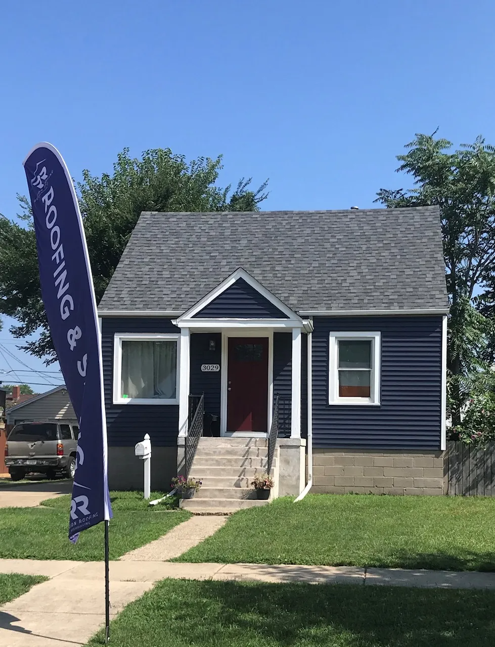 A blue house with a roofing flag in front of it