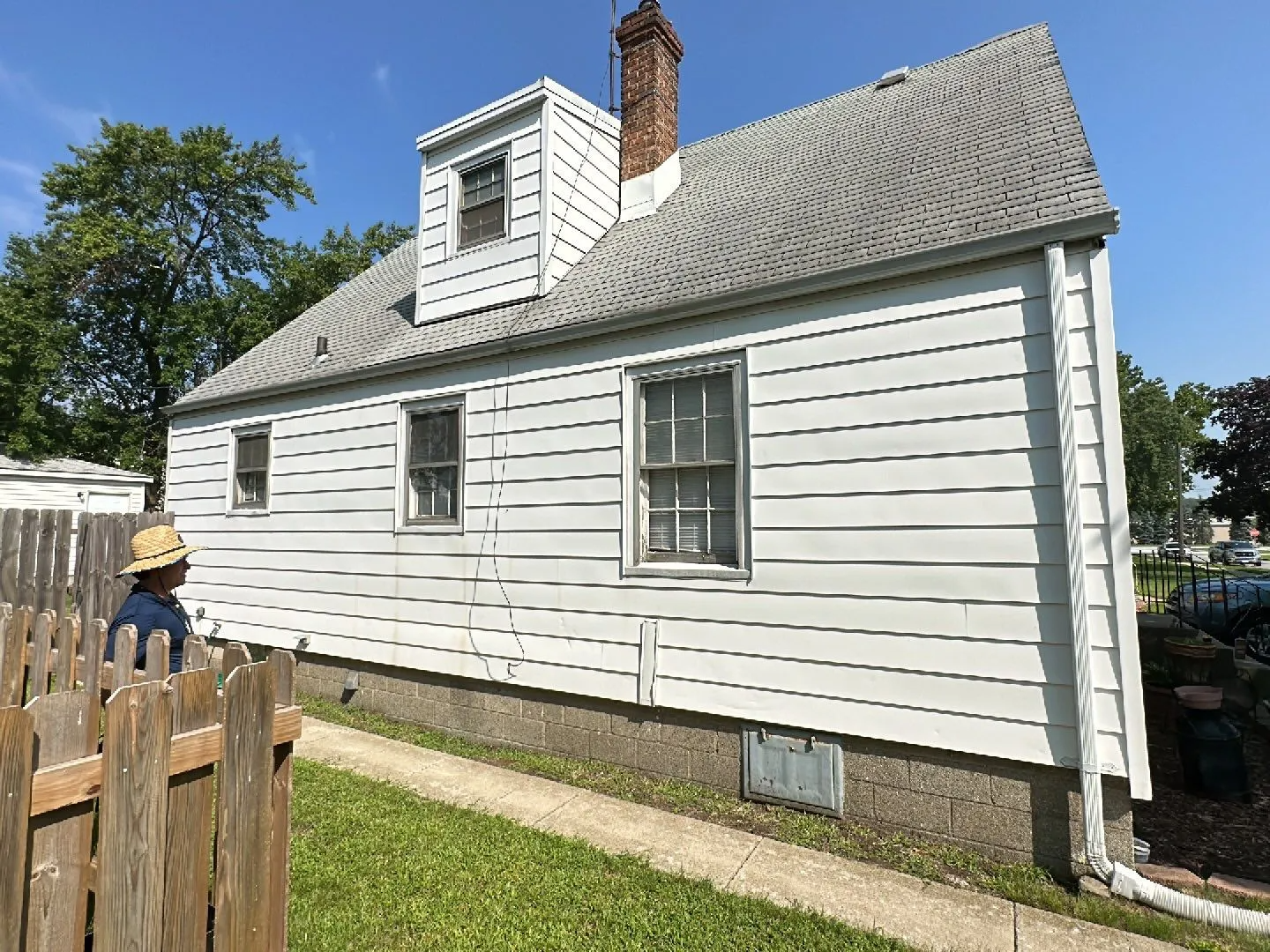 A man in a hat is standing in front of a white house.