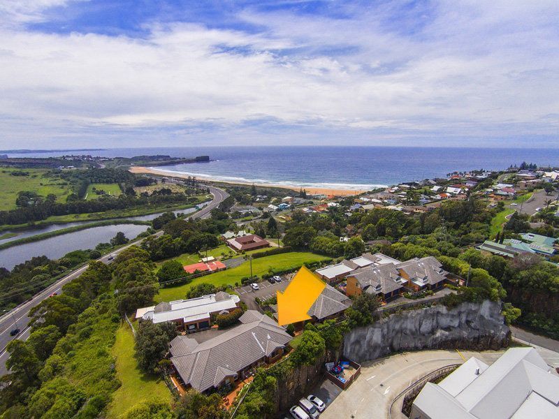 Aerial view of buildings on a hill overlooking a beach and ocean under a cloudy sky.