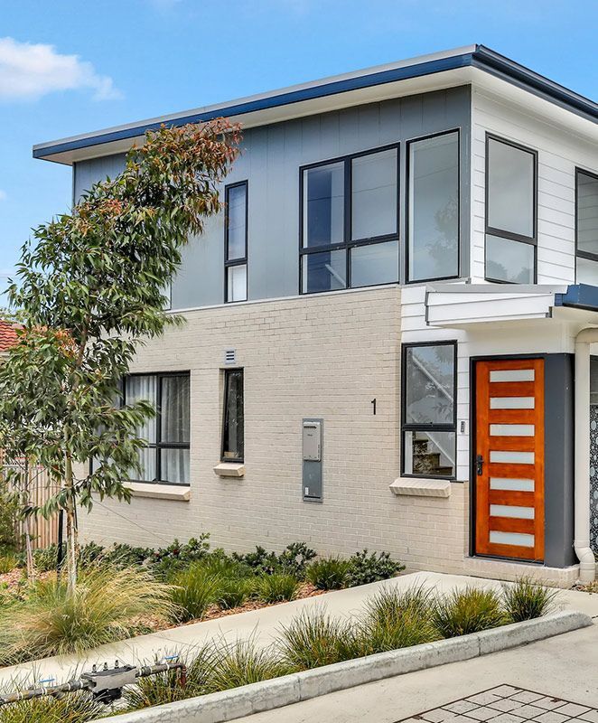 Two-story modern home with brick exterior, large windows, and a wooden door.