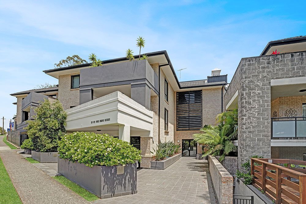 Multi-story apartment building with light and dark gray and tan exteriors and a small entry garden.