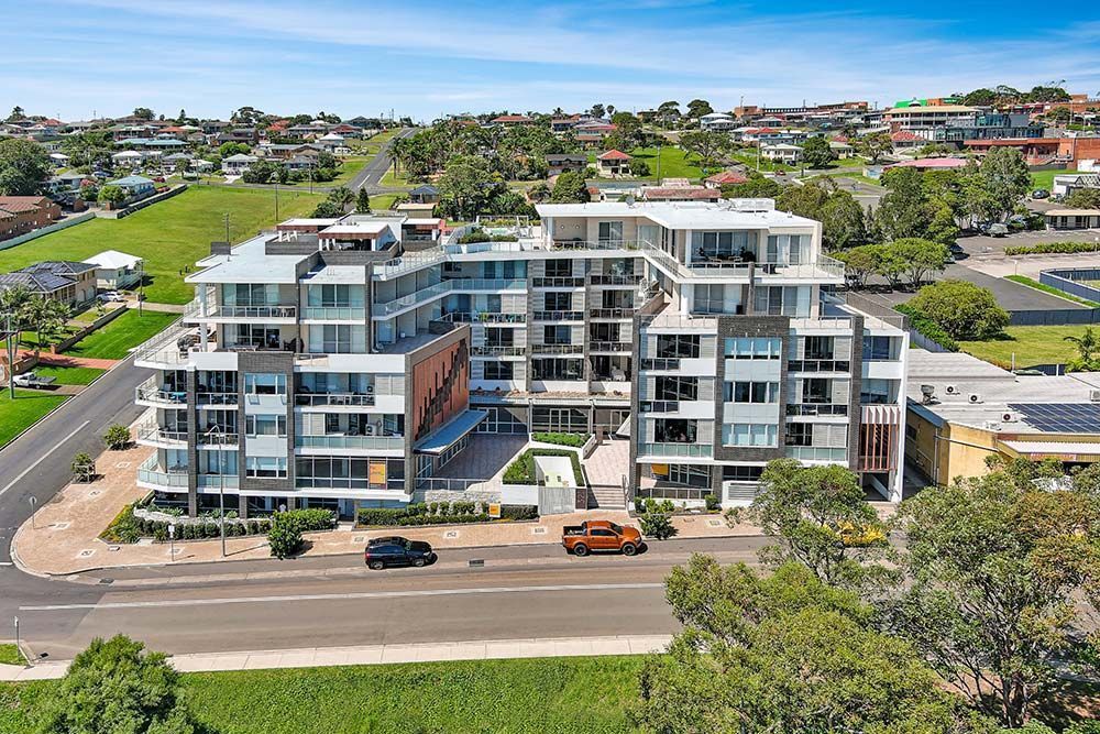 Modern apartment building with multiple balconies and rooftop terraces, in a suburban area.